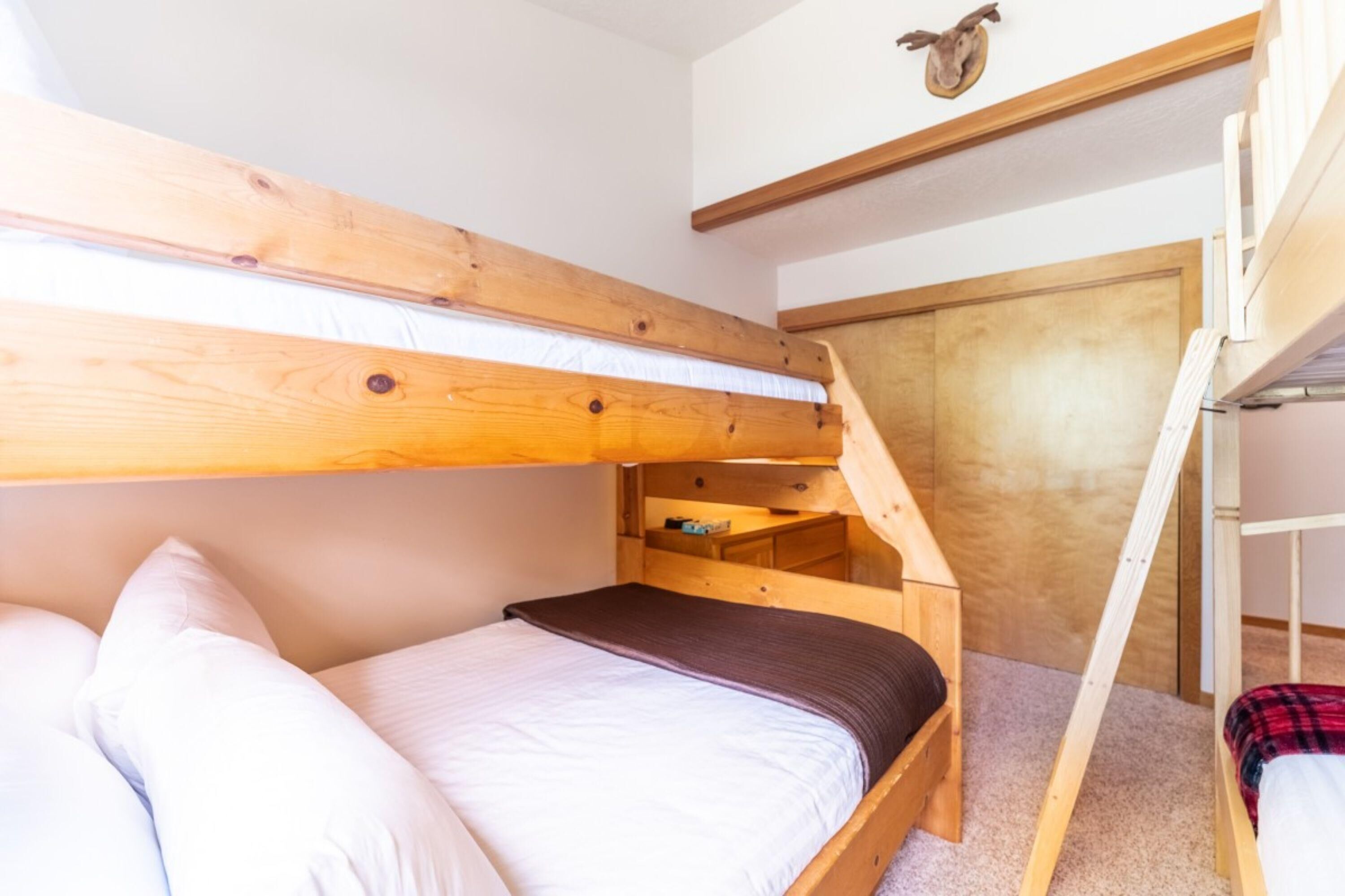 Habitación con literas, cabecera de madera, un estante pequeño debajo de la cama y una escalera de madera.
