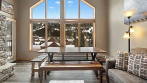 A spacious room with a large wooden table and benches, a stone fireplace, and a large window offering a view of a snowy mountain landscape. - Gw5095-3 (Keystone)