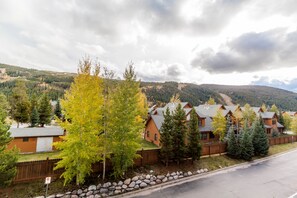 Houses with a rustic aesthetic sit amidst a well-manicured lawn and stone wall, surrounded by trees in a hilly area.