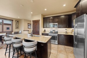 Una cocina moderna con armarios de madera oscura, electrodomésticos de acero inoxidable y una isla de encimera de granito con taburetes de bar.