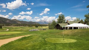 Un campo de golf con una carpa, un edificio y montañas al fondo.