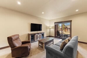 Una sala de estar con televisor de pantalla plana, sillón de cuero, sofá gris y una mesa de centro de madera.