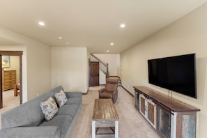 A living room with a grey sofa, a wooden coffee table, a brown armchair, and a TV on a wooden cabinet.