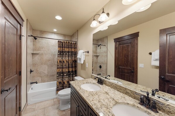 A modern bathroom with a bathtub, two sinks, a large mirror, and a shower with patterned curtains.