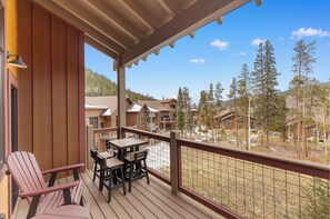 A wooden deck with a table and chairs, overlooking a resort area with multiple buildings and trees. - Alders #801 by Summit County Mountain Retreats (Keystone)