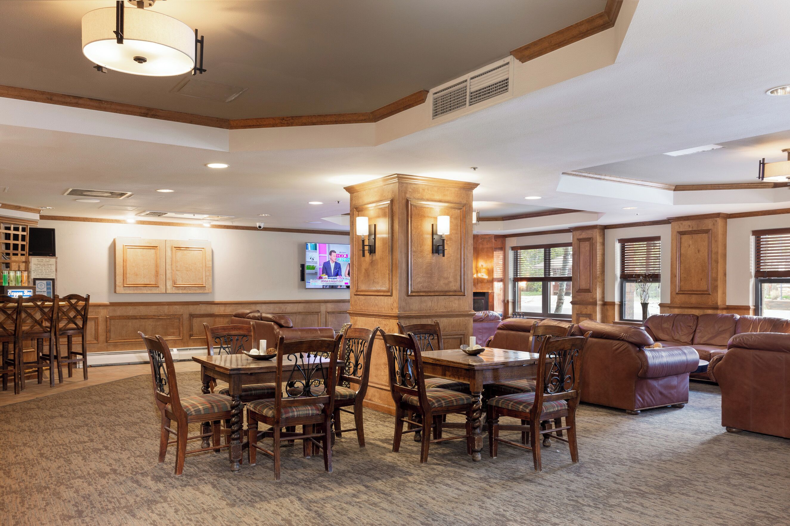 A spacious lobby with a wooden dining table surrounded by chairs, a leather sofa, and a television mounted on the wall.