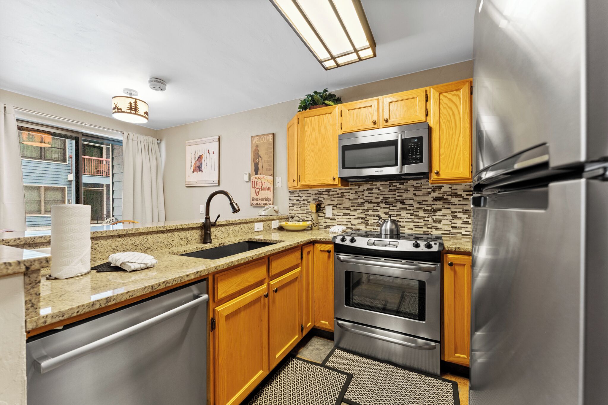 A modern kitchen with wooden cabinets, stainless steel appliances, a granite countertop, and a patterned backsplash.