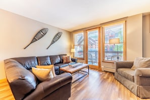 A living room with a brown leather sofa, a grey armchair, a wooden coffee table, and two windows with blinds. - Bb8046-2 (Keystone)