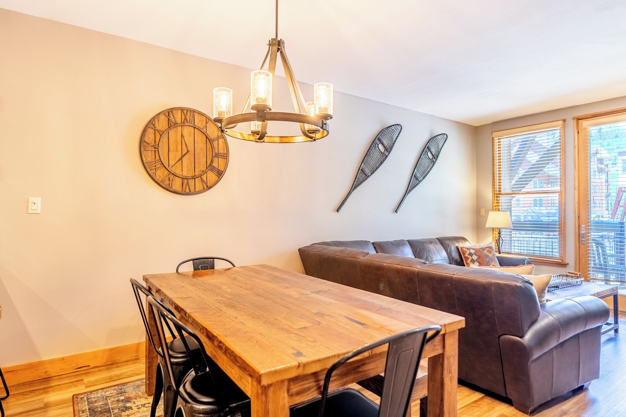 A dining area with a wooden table and chairs, a brown leather sofa, a chandelier, and two wall-mounted fish-shaped decorations.