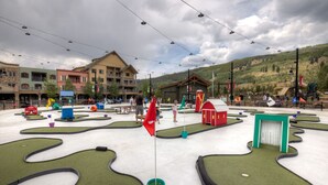 A miniature golf course with artificial turf, surrounded by buildings and a mountainous backdrop. - Silver Mill by Summit County Mountain Retreats (Keystone)