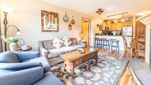 A living room with a sofa, coffee table, and a rug. There is a kitchen area with a refrigerator, microwave, and bar stools. - Silver Mill by Summit County Mountain Retreats (Keystone)
