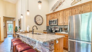 A kitchen with a large island, wooden cabinets, stainless steel appliances, and a stone countertop. - Jackpine Lodge by Summit County Mountain Retreats (Keystone)