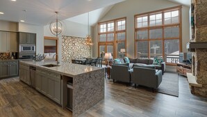 A spacious kitchen with a large island, a dining area with a table and chairs, a living room with a sofa and a fireplace, and large windows providing natural light. - Lone Eagle by Summit County Mountain Retreats (Keystone)