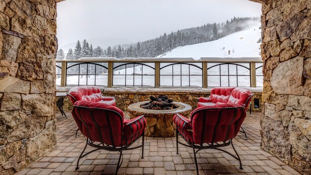 A stone-walled room with a stone fire table and two red chairs, overlooking a snowy mountain slope. - Lone Eagle by Summit County Mountain Retreats (Keystone)