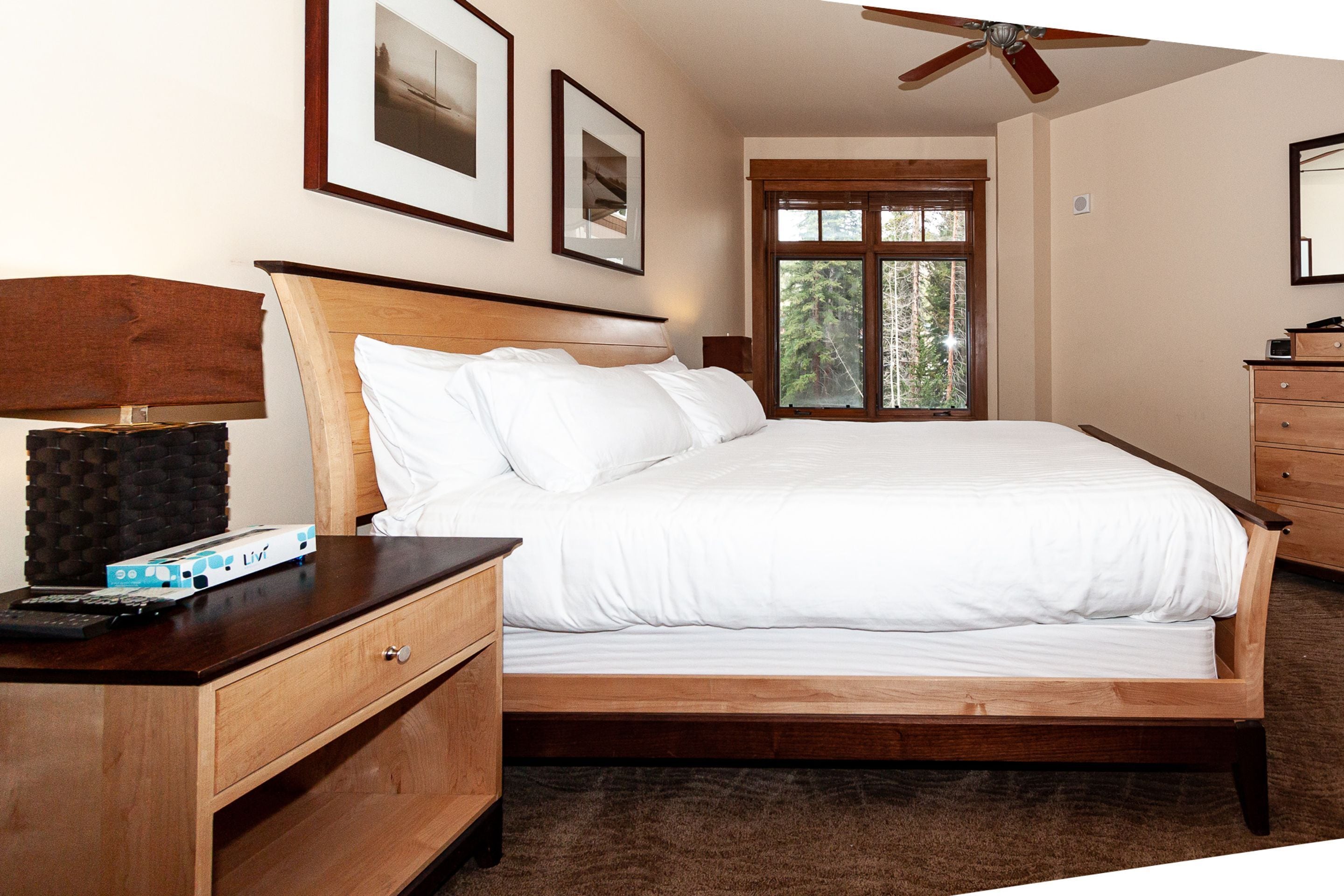 Un dormitorio con una cama de madera, una mesita de noche con lámpara, un aparador y cuadros enmarcados en la pared.