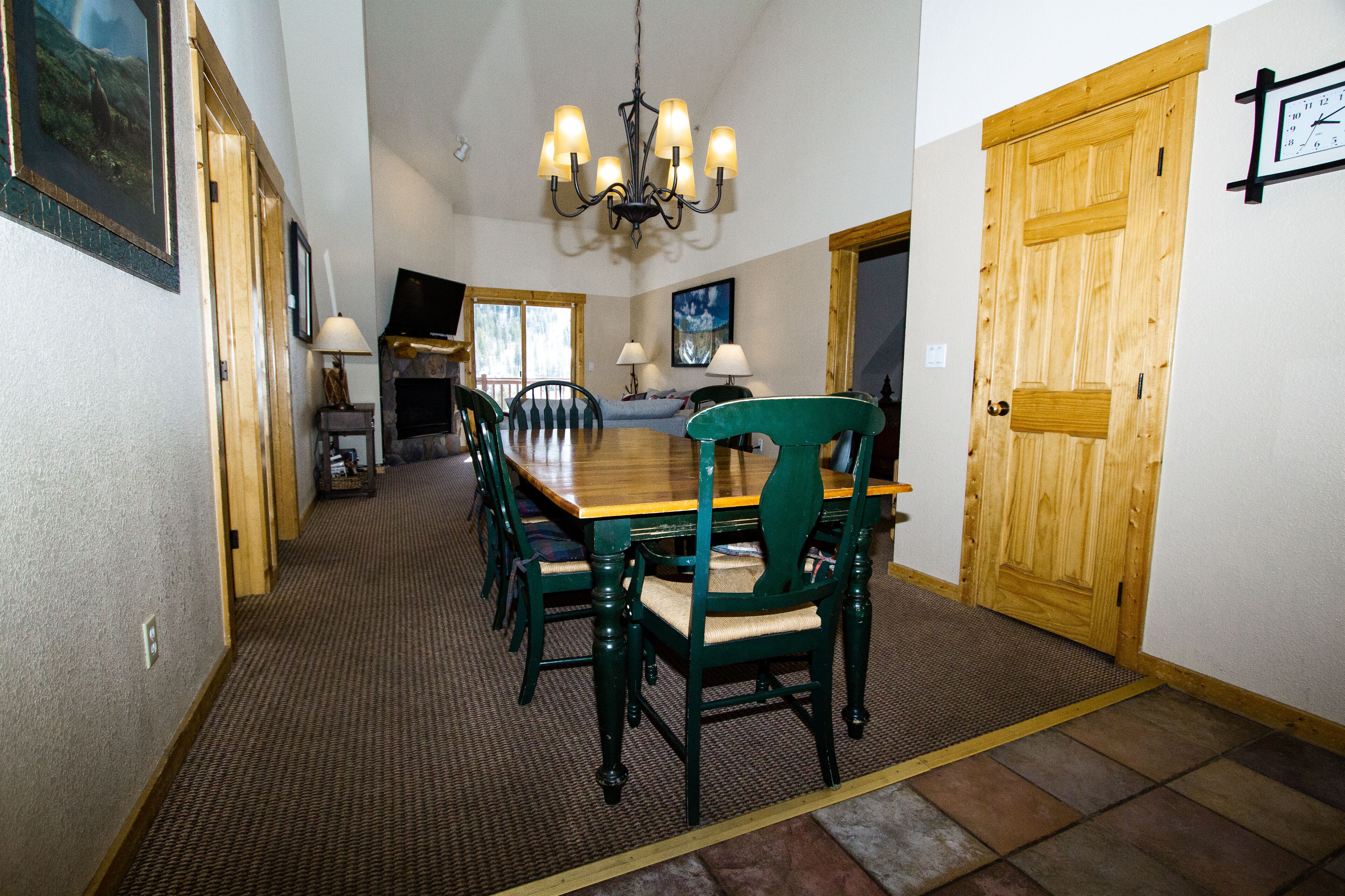 A dining area with a wooden table, green chairs, a chandelier, and a wooden door.