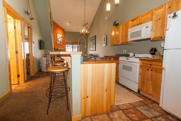 A kitchen with wooden cabinets, a microwave, a stove, and a bar area with stools. - Tenderfoot Lodge by Summit County Mountain Retreats (Keystone)