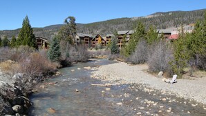 Une rivière traverse une zone de villégiature où se trouvent des bâtiments d’hébergement et une chaise est placée sur la rive.