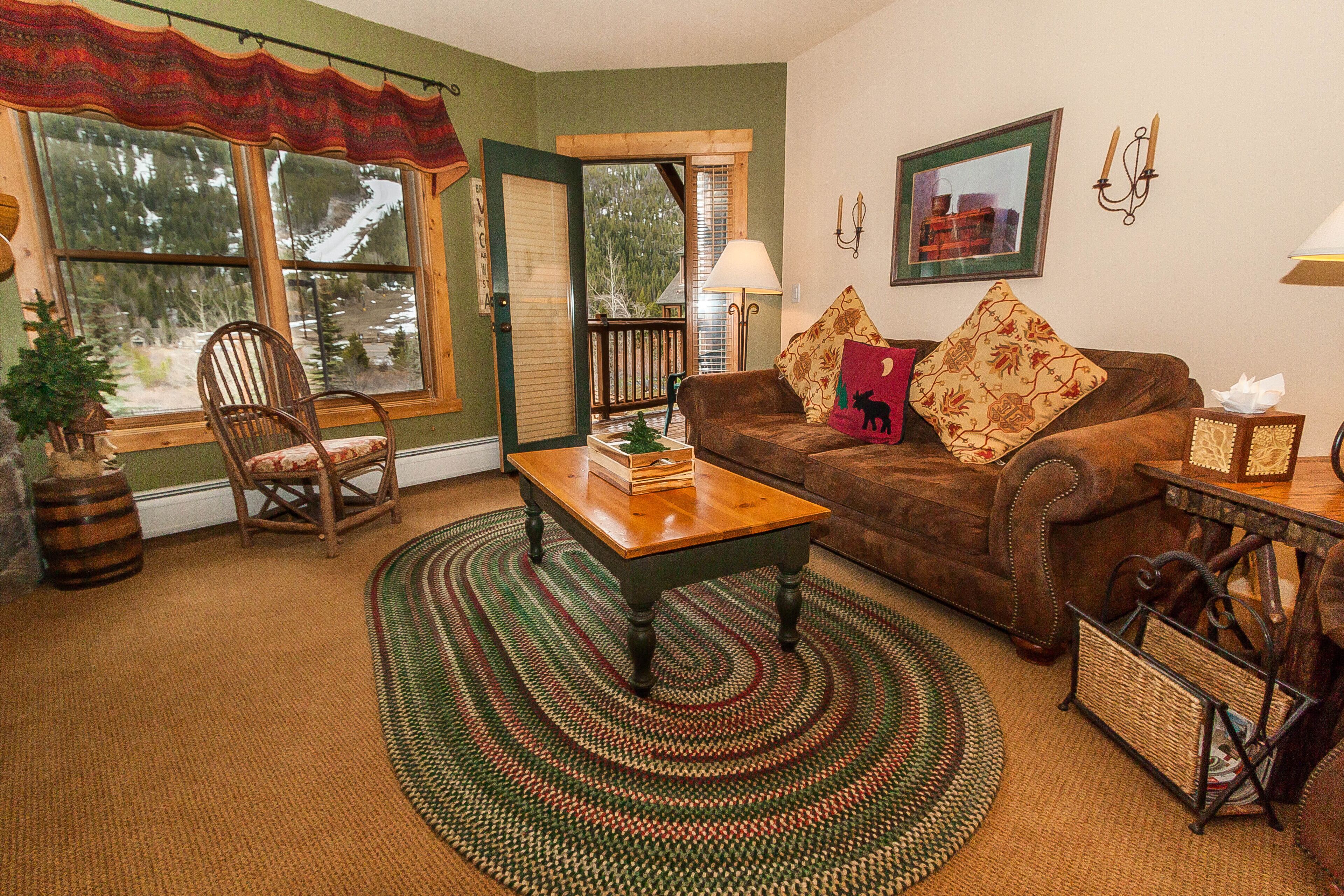 A cozy living room with a brown leather sofa, a wooden coffee table, and a green patterned rug.