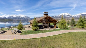 Un pabellón de madera con bancos y chimenea, con vistas a un lago y montañas.