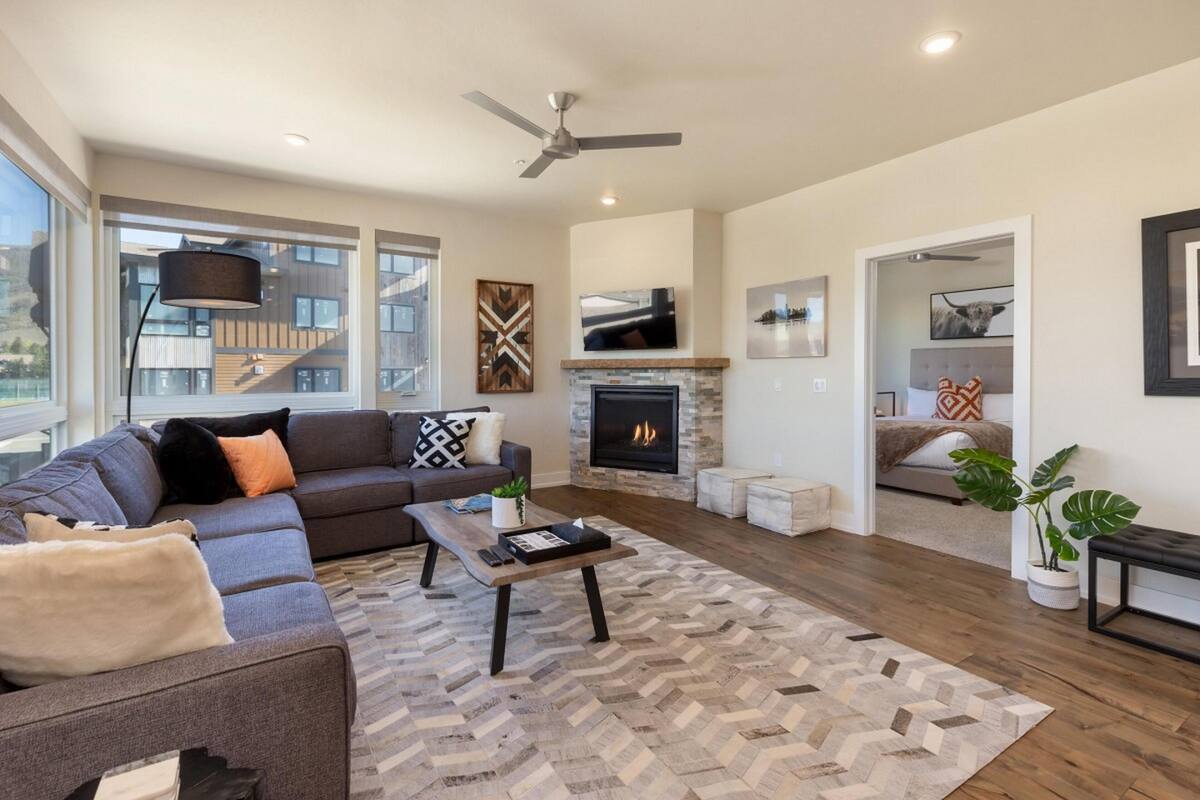 A modern living room with a sofa, coffee table, fireplace, and large windows.