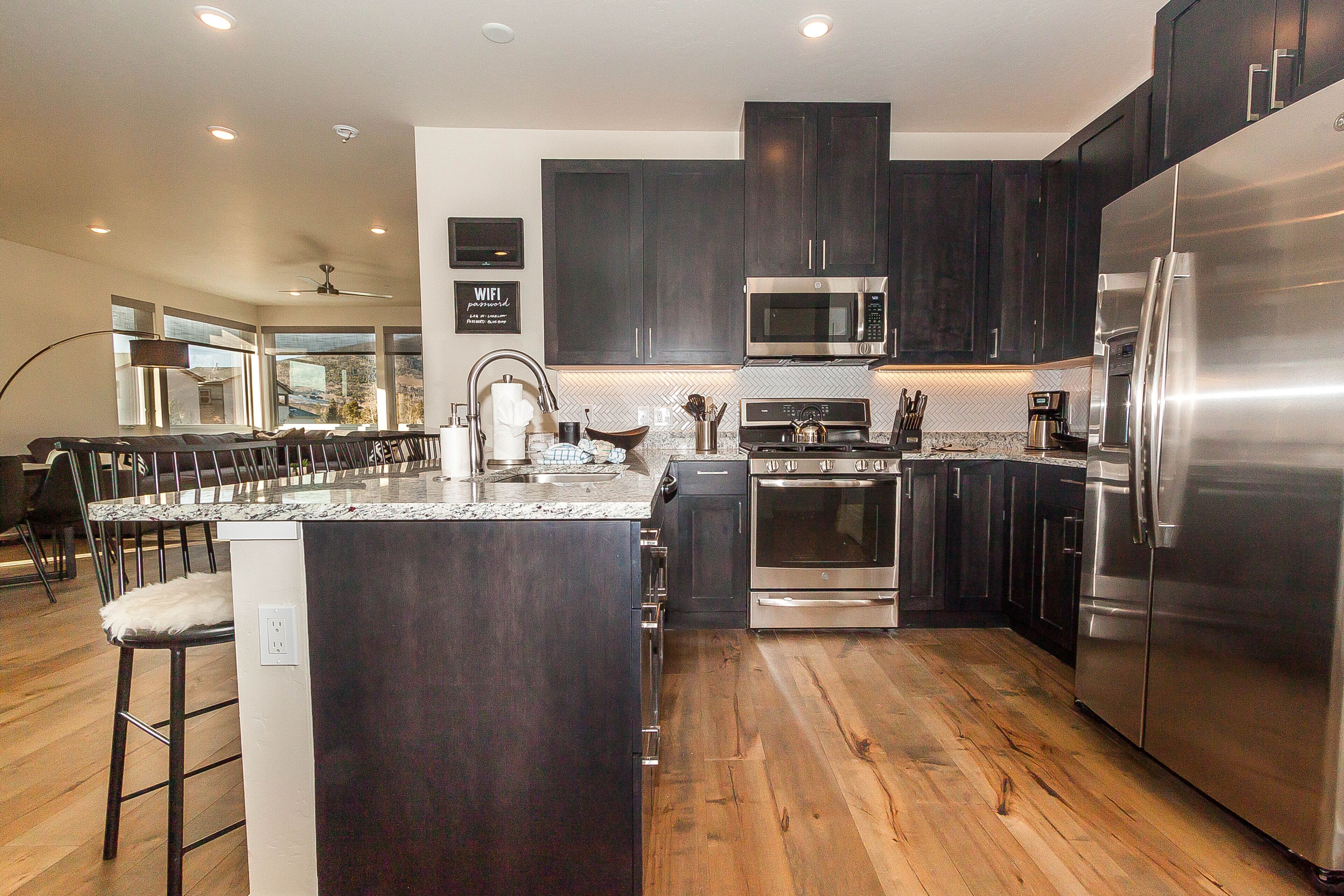 A modern kitchen with dark cabinets, stainless steel appliances, and a wooden floor.