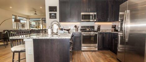 A modern kitchen with dark cabinets, stainless steel appliances, and a wooden floor.