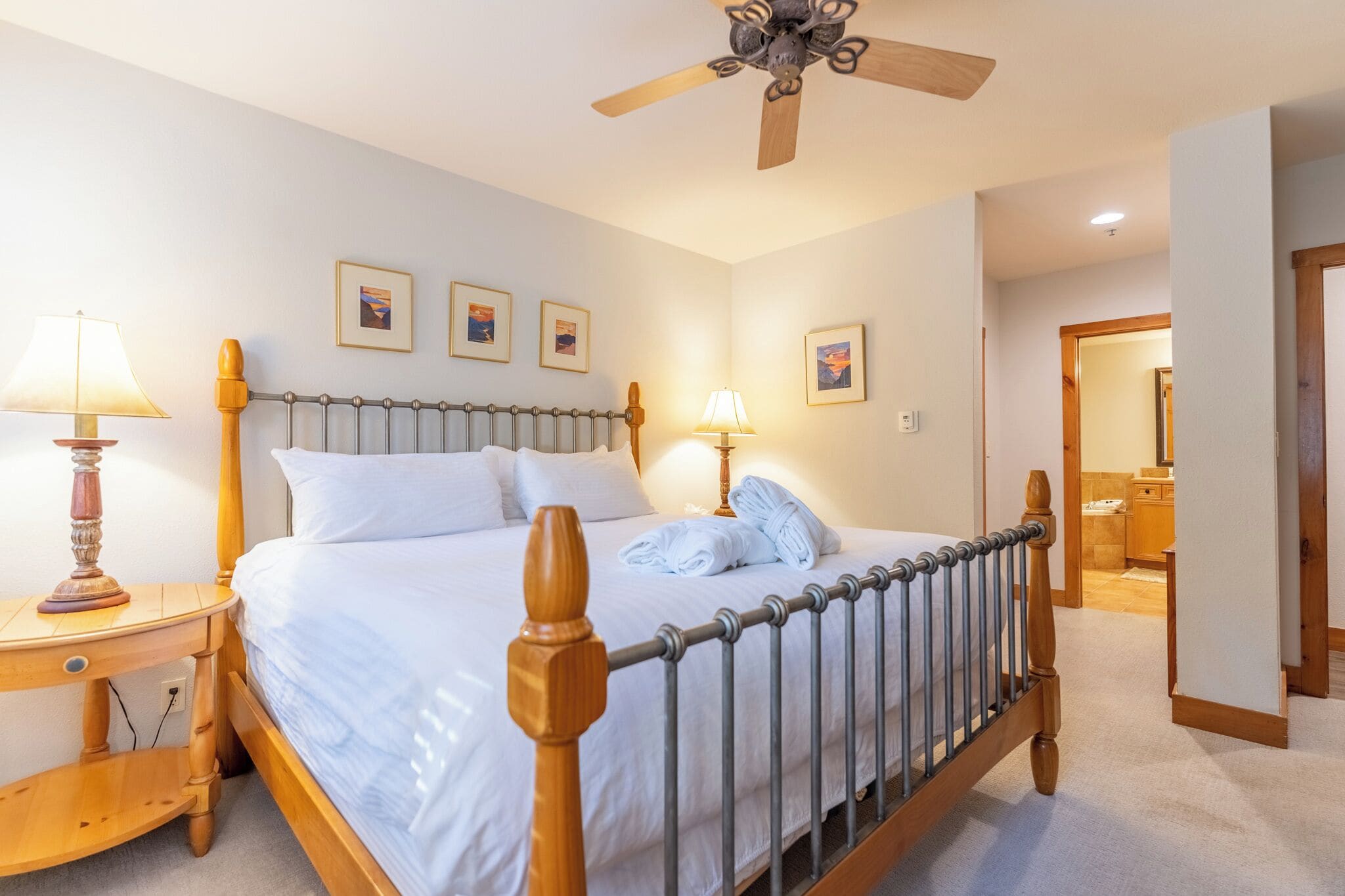Een keurig opgemaakt bed met een houten hoofdbord en metalen leuningen, twee bedlampen en ingelijste foto's aan de muur.