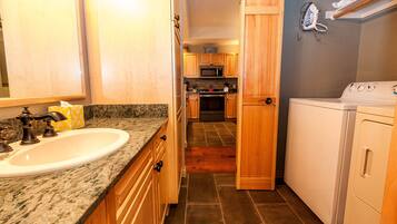 A compact kitchen with a granite countertop, stainless steel sink, wooden cabinets, a microwave, oven, and a washing machine.