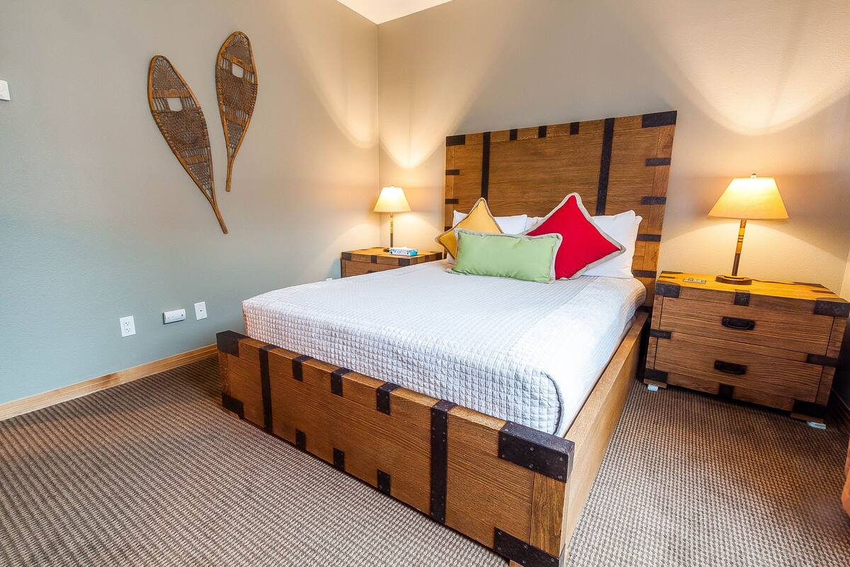 A neatly made bed with a wooden headboard, two bedside tables with lamps, and decorative wall art.