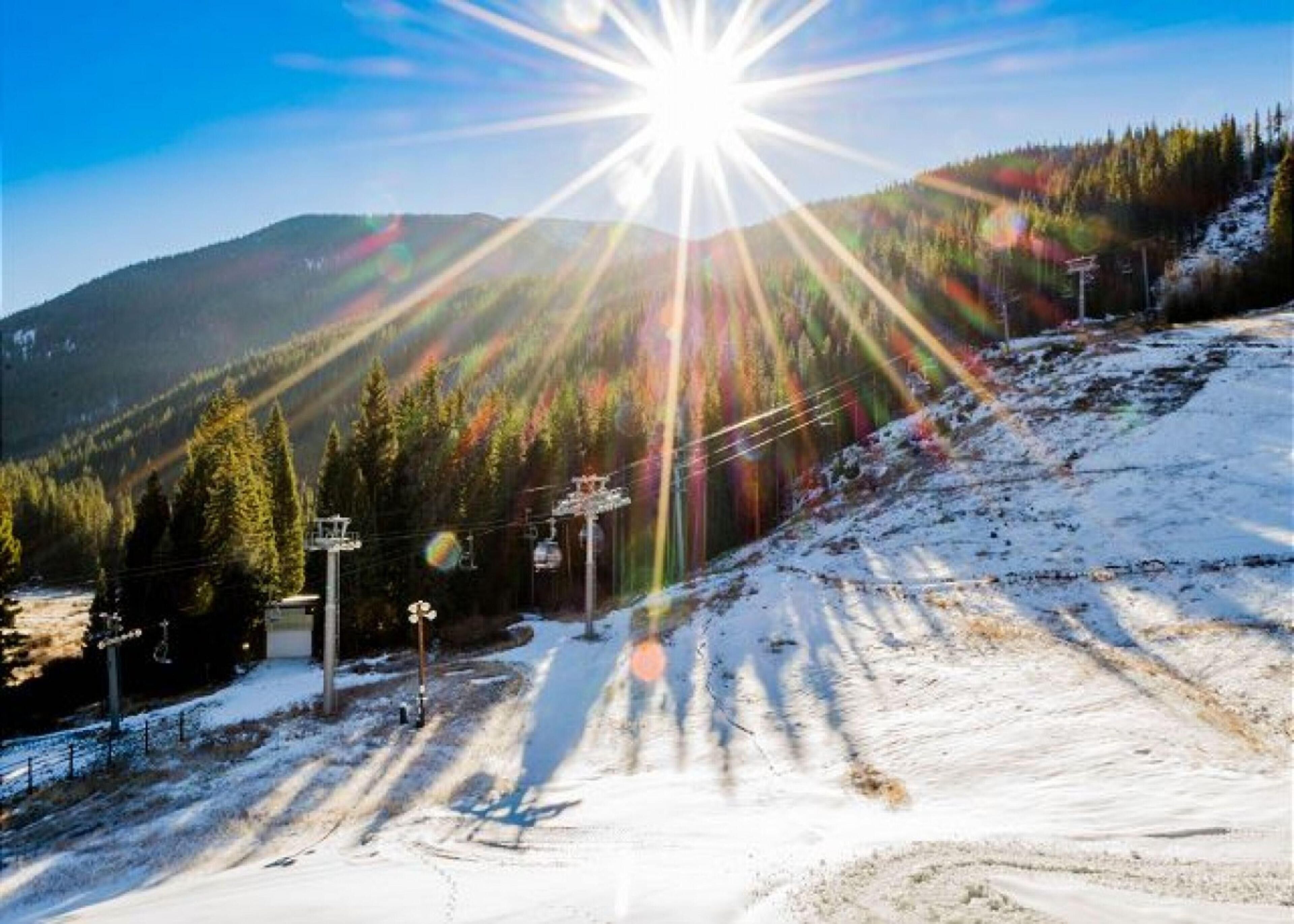 Una pista da sci innevata con il sole che splende, circondata da alberi e montagne.