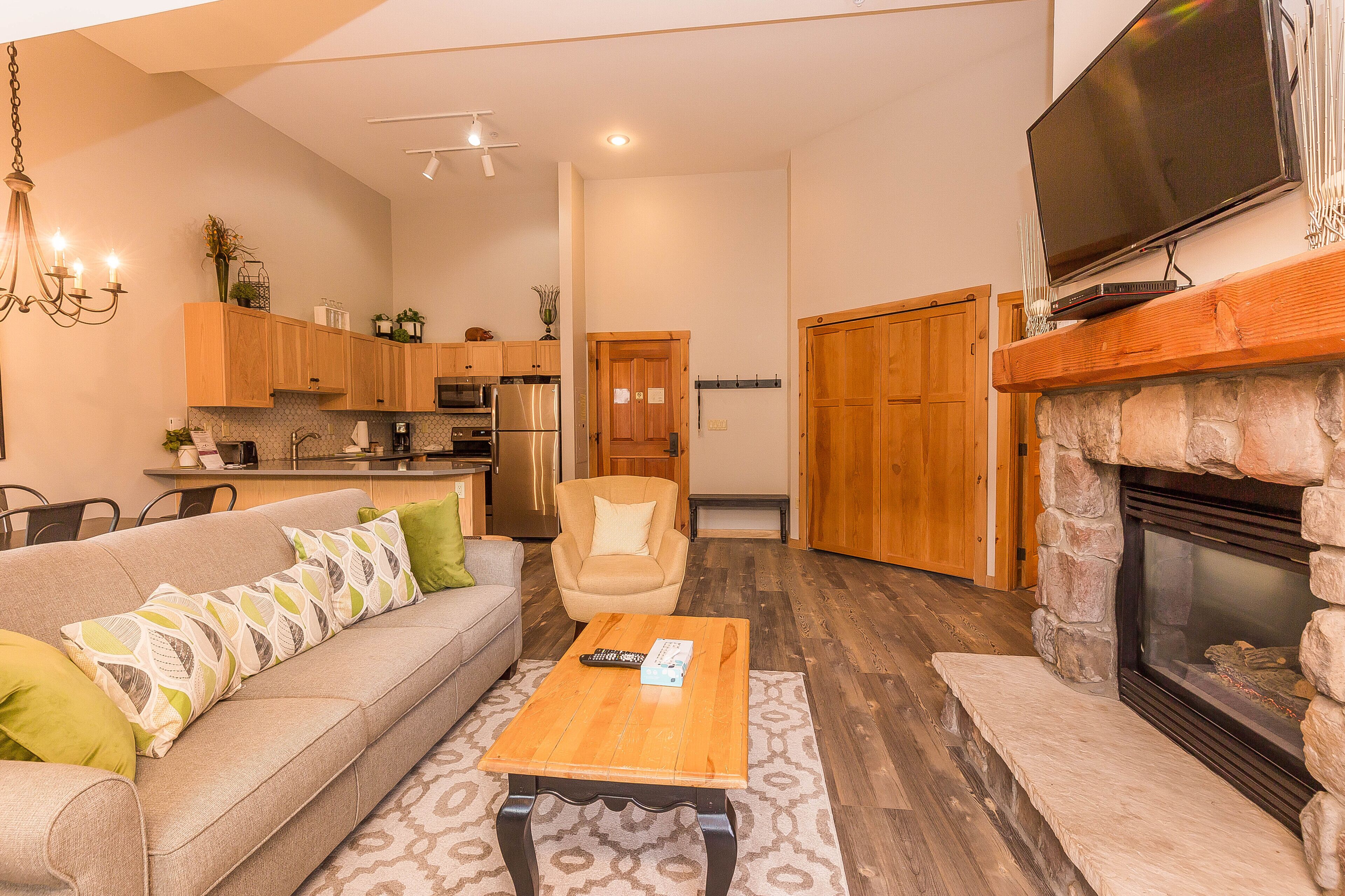 A modern living room with a sofa, coffee table, fireplace, and kitchen in the background.