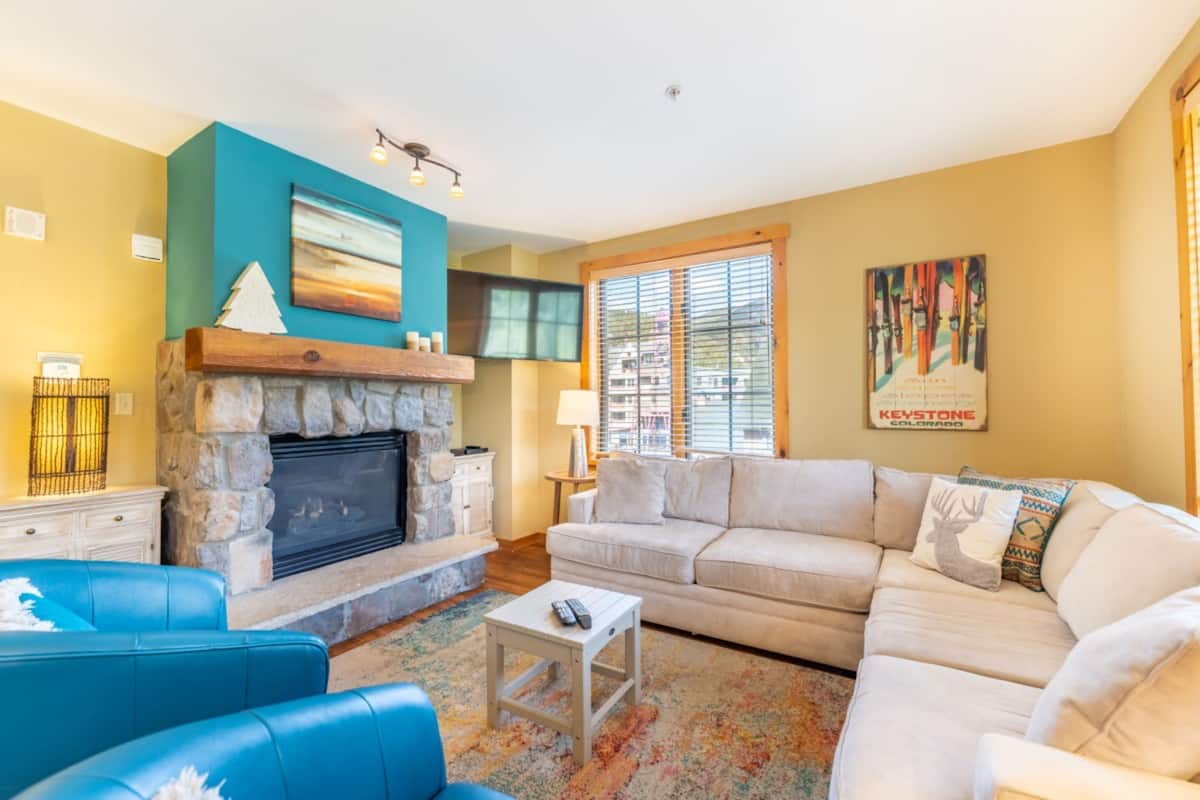 A living room with a stone fireplace, a beige sofa, and a blue armchair.