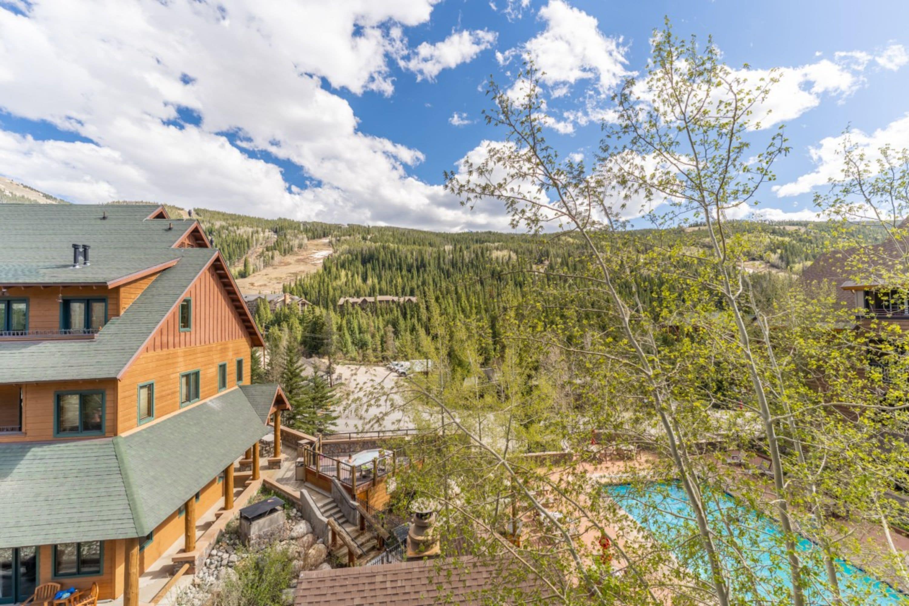 A lodge with a pool, wooden exterior, and a mountainous backdrop.