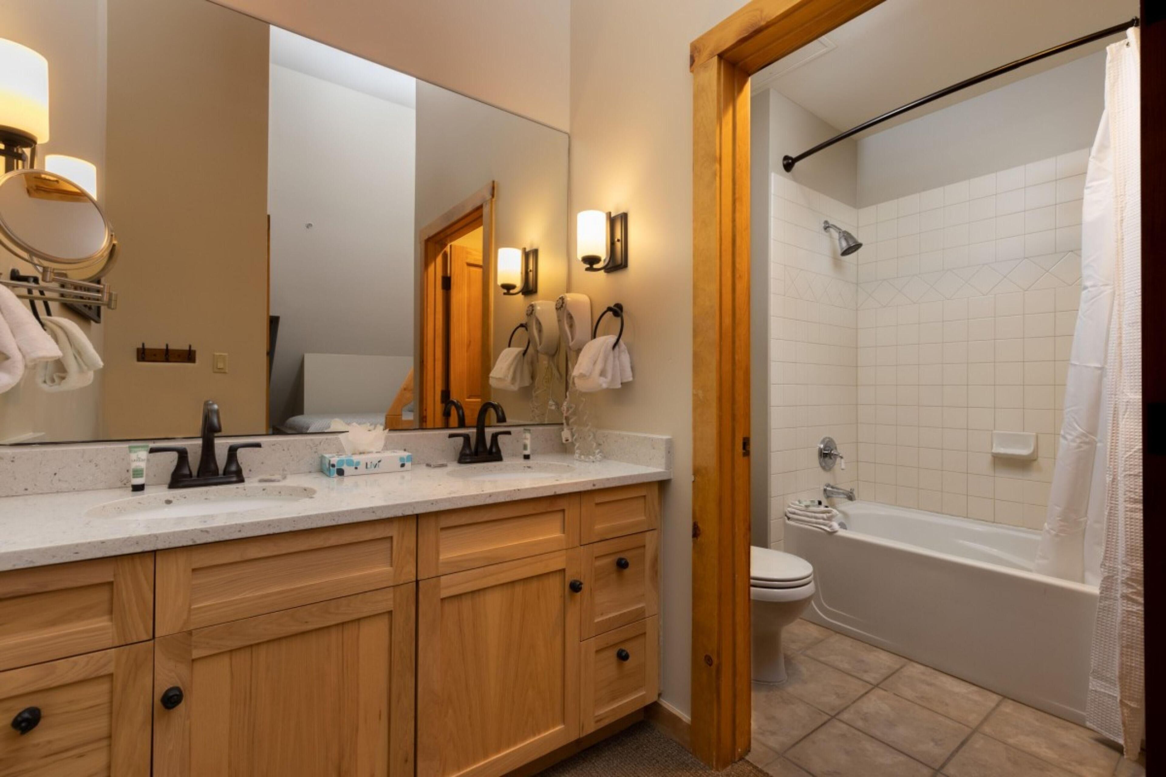 A bathroom with a wooden vanity, a large mirror, a bathtub, and a shower area.