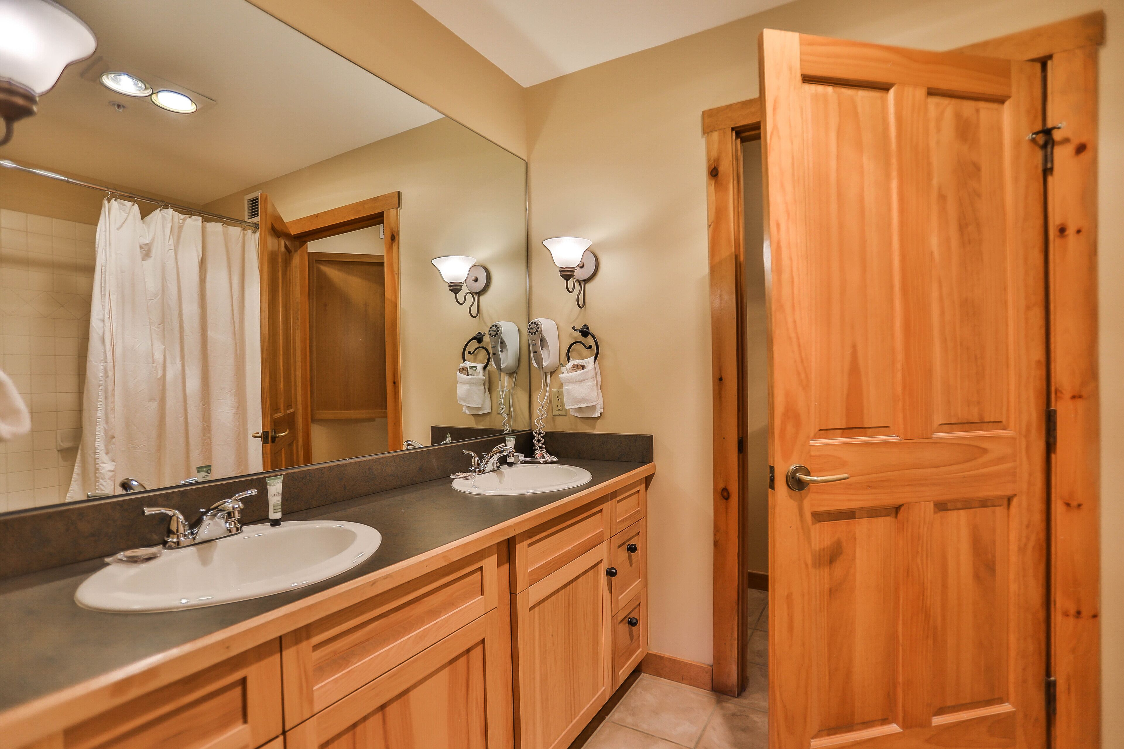A bathroom with two sinks, wooden cabinets, a large mirror, and a wooden door.