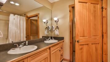 A bathroom with two sinks, wooden cabinets, a large mirror, and a wooden door.