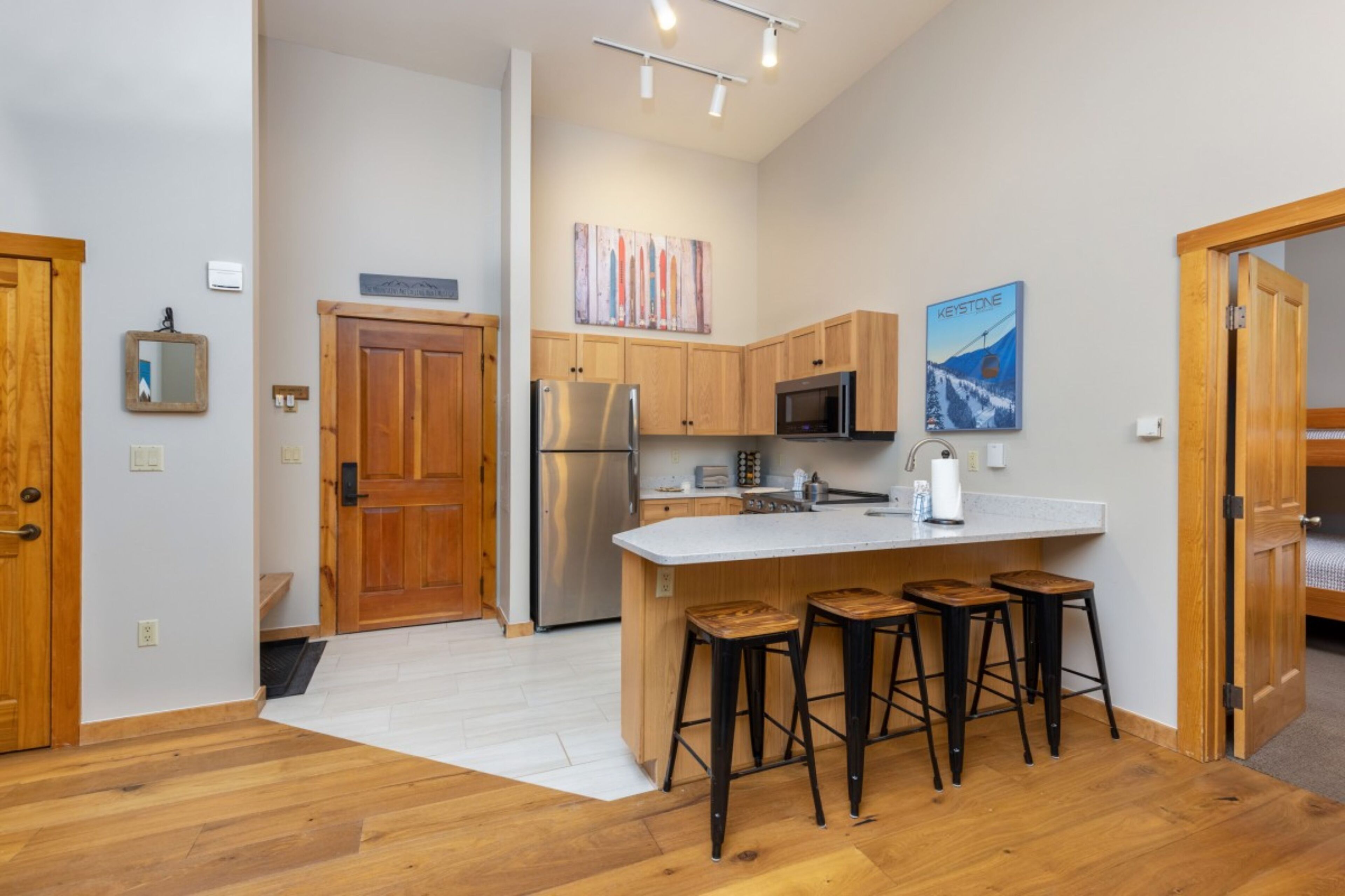 A modern kitchen with wooden cabinets, a stainless steel refrigerator, a microwave, and a large island with bar stools.