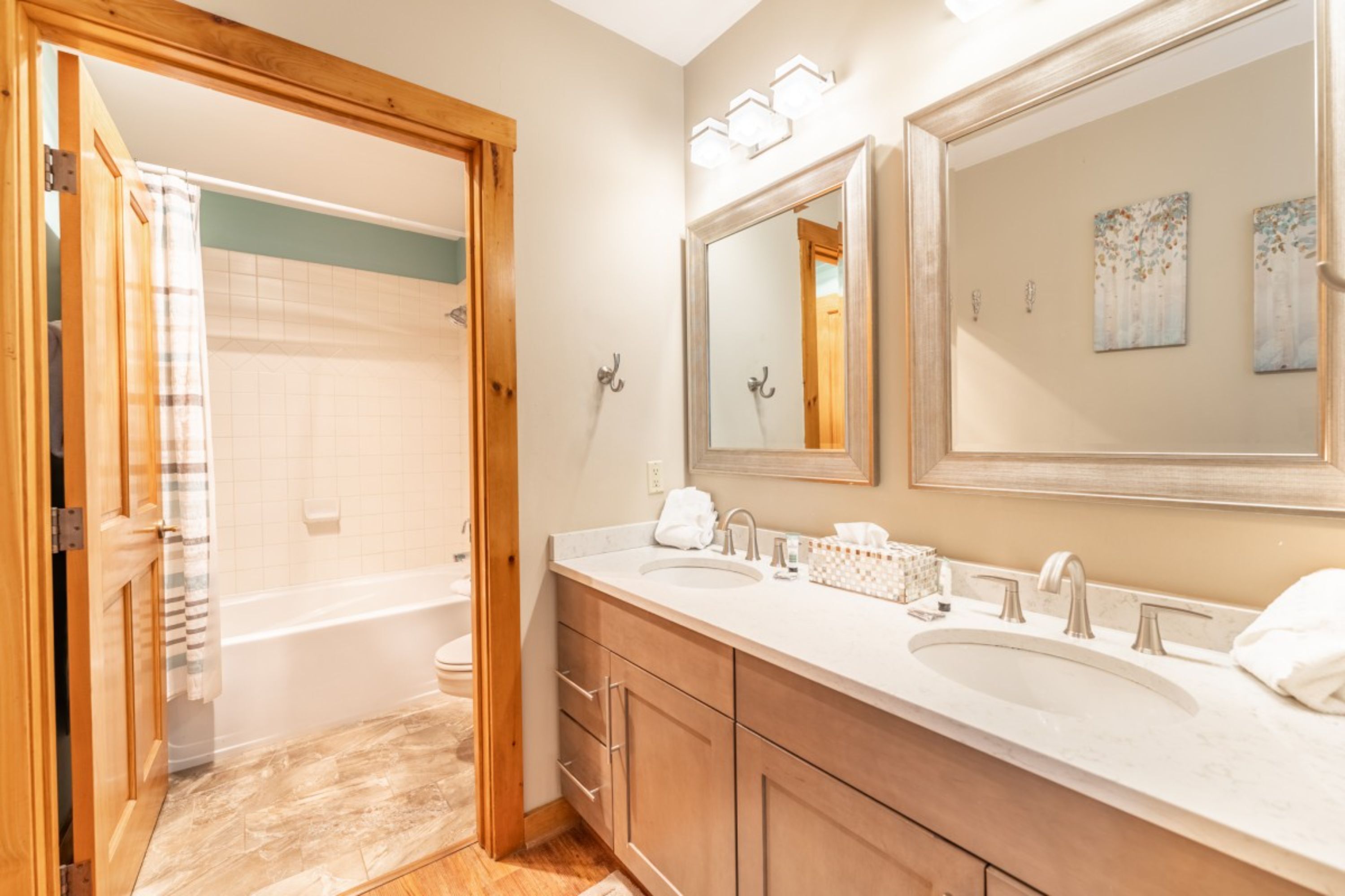 A bathroom with a wooden vanity, two sinks, a large mirror, and a shower area.