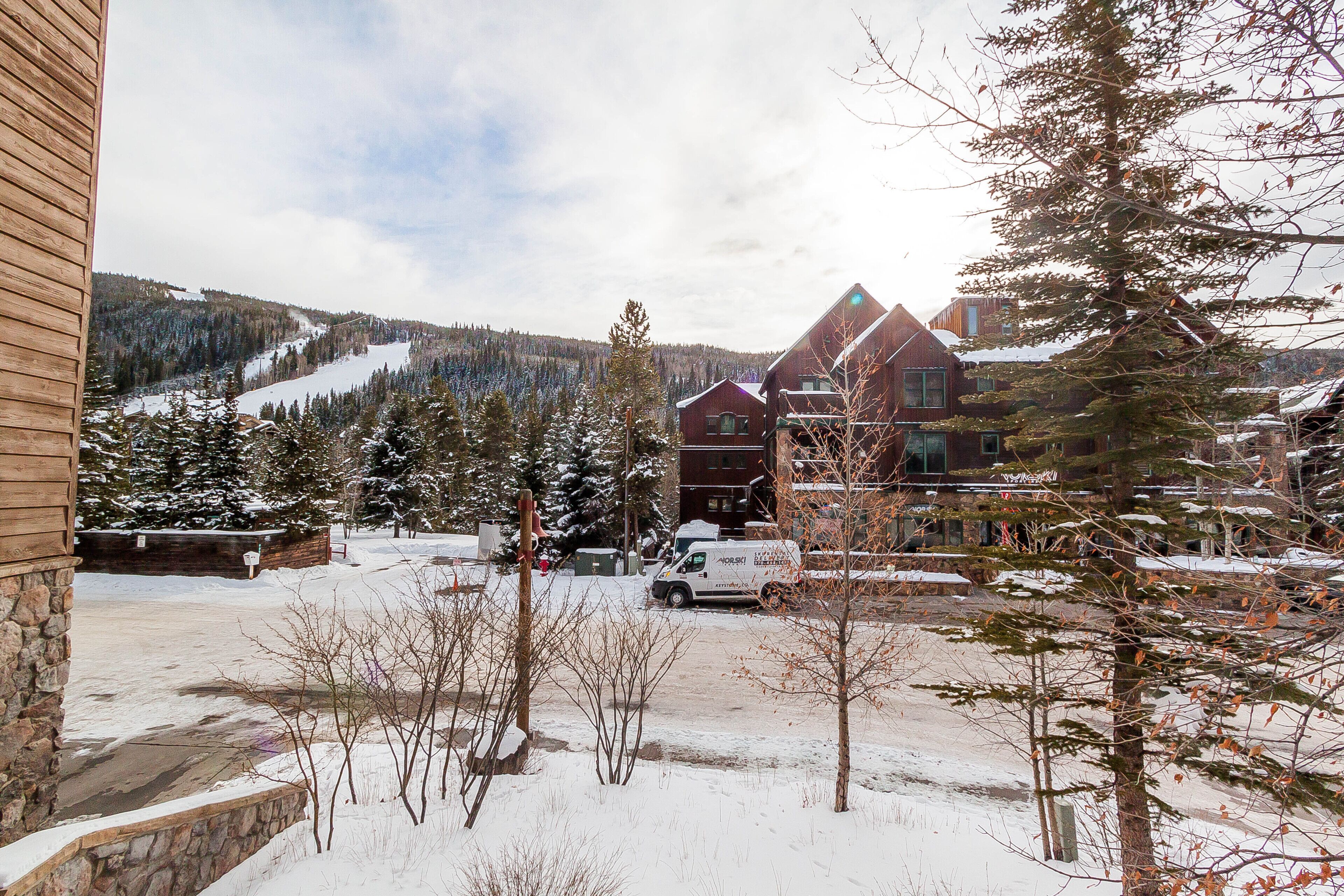 A snow-covered landscape with a lodge, a parking area, and a mountain in the background.