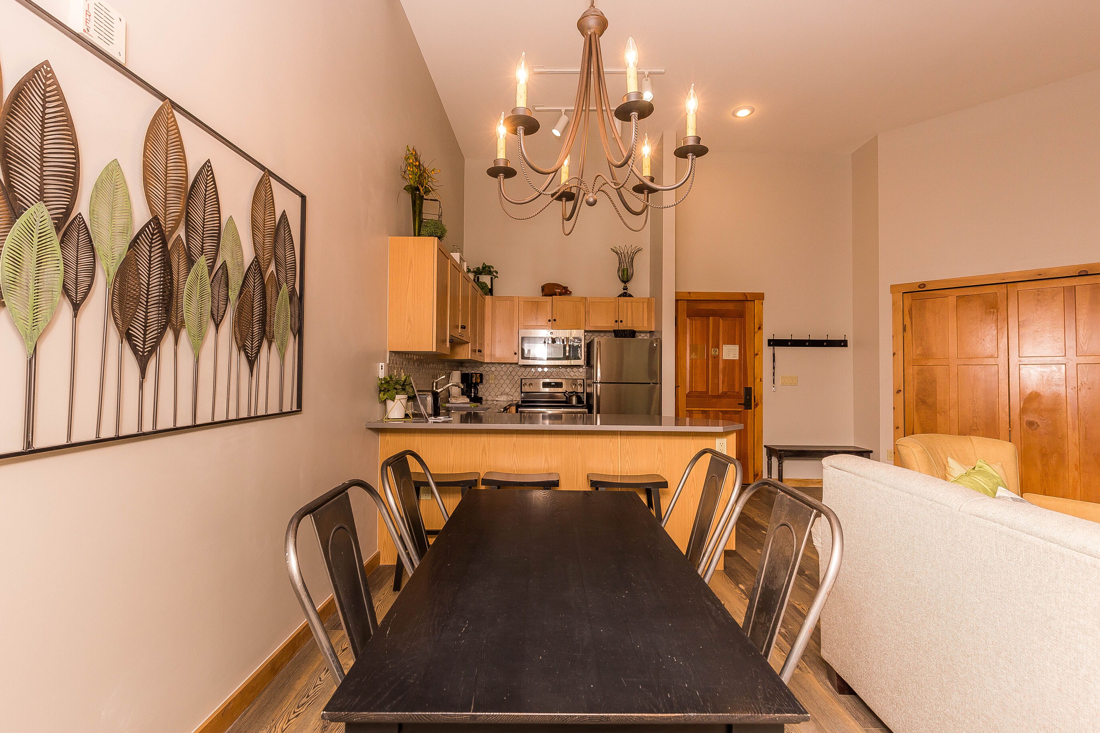 Un espace repas avec une longue table, des chaises, un lustre et une cuisine en arrière-plan.
