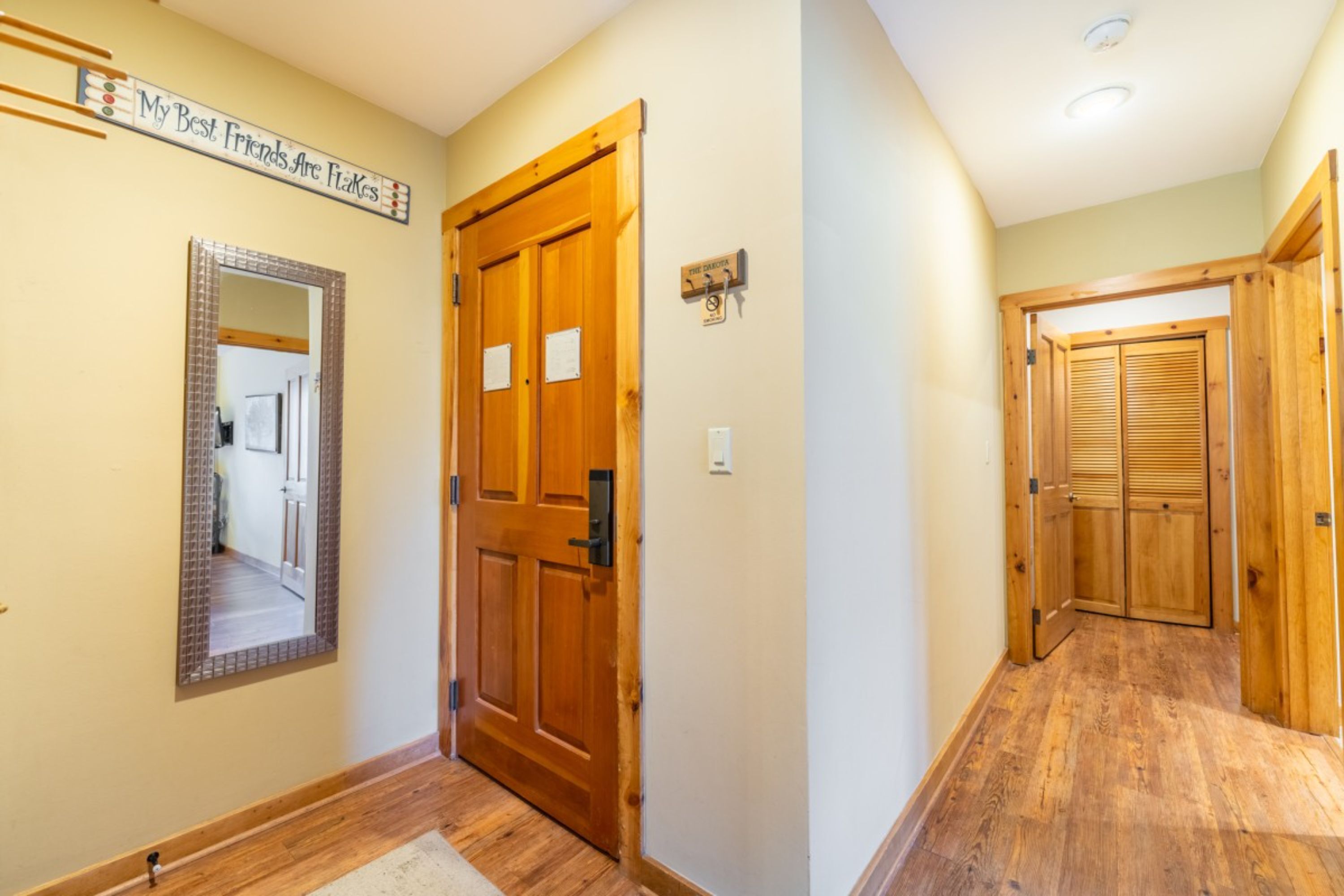 A hallway with wooden doors, a mirror, and a sign that reads "My Best Friends Are Fakes".