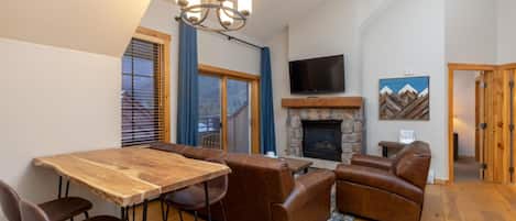 A spacious living area with a wooden dining table, leather sofas, and a stone fireplace.
