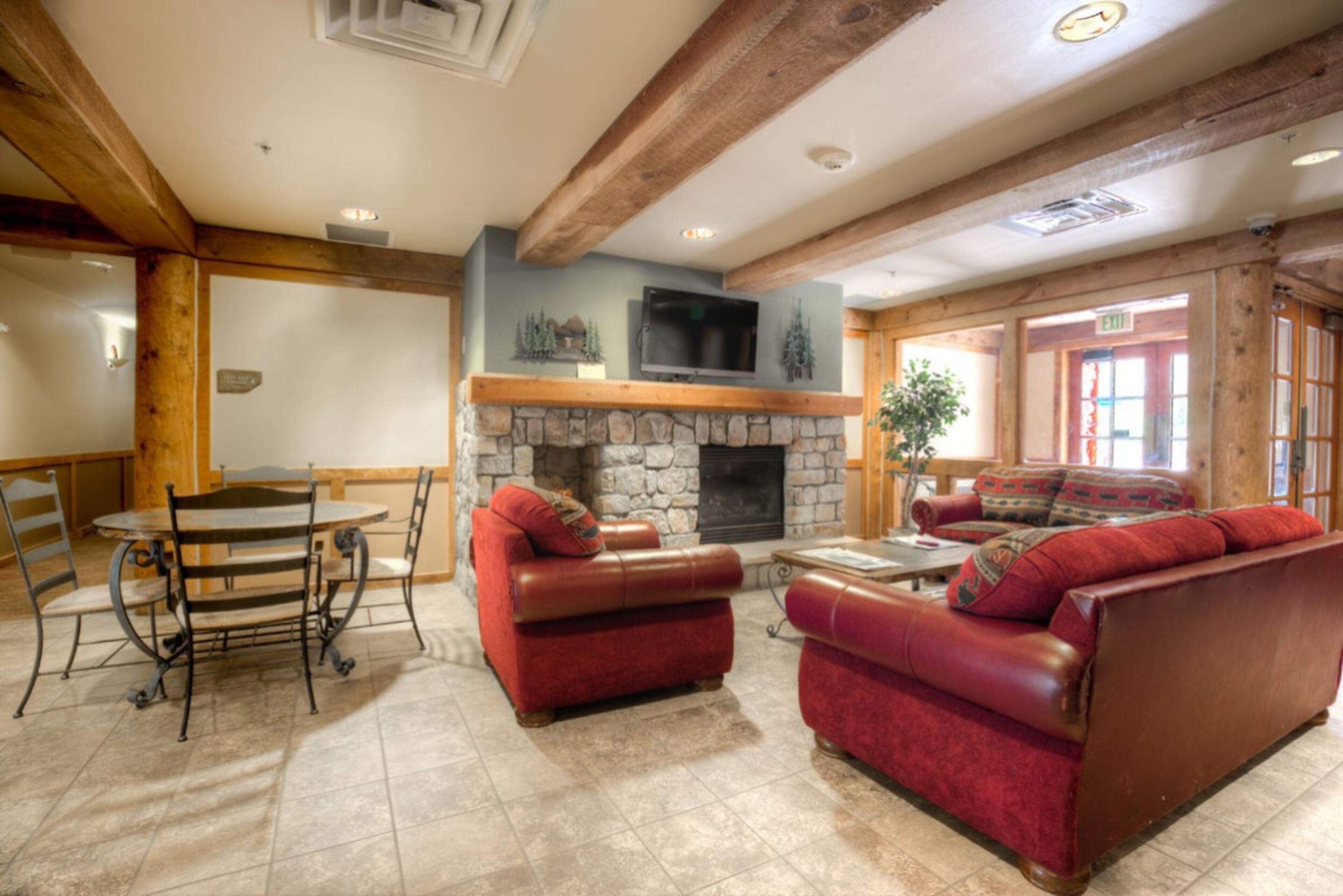A cozy lounge area with a stone fireplace, leather sofas, a round table, and a television mounted above the fireplace.