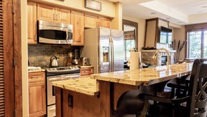 A kitchen with wooden cabinets, stainless steel appliances, a granite countertop, and a built-in island with bar seating. - Crystal Peak Lodge by Summit County Mountain Retreats (Breckenridge)