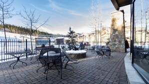 An outdoor patio with brick flooring and metal chairs, overlooking a snowy landscape and a ski lift. - Crystal Peak Lodge by Summit County Mountain Retreats (Breckenridge)