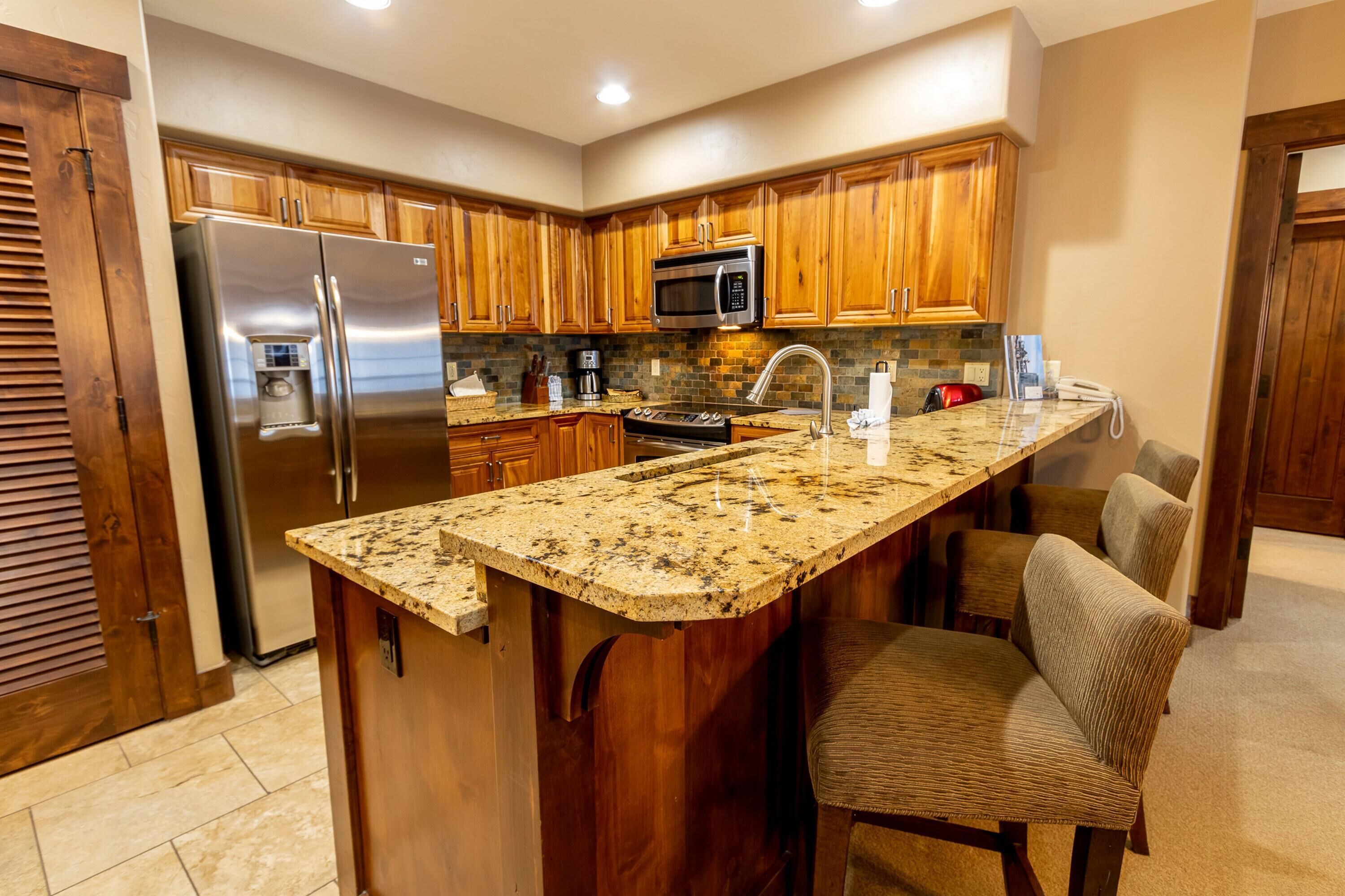 Una cocina con armarios de madera, electrodomésticos de acero inoxidable, encimera de granito y una zona de bar con asientos.