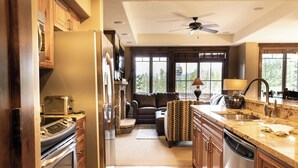 A modern kitchen with a built-in oven, microwave, and dishwasher, a dining area with a table and chairs, and a large window offering a view of the outdoors. - Crystal Peak Lodge by Summit County Mountain Retreats (Breckenridge)