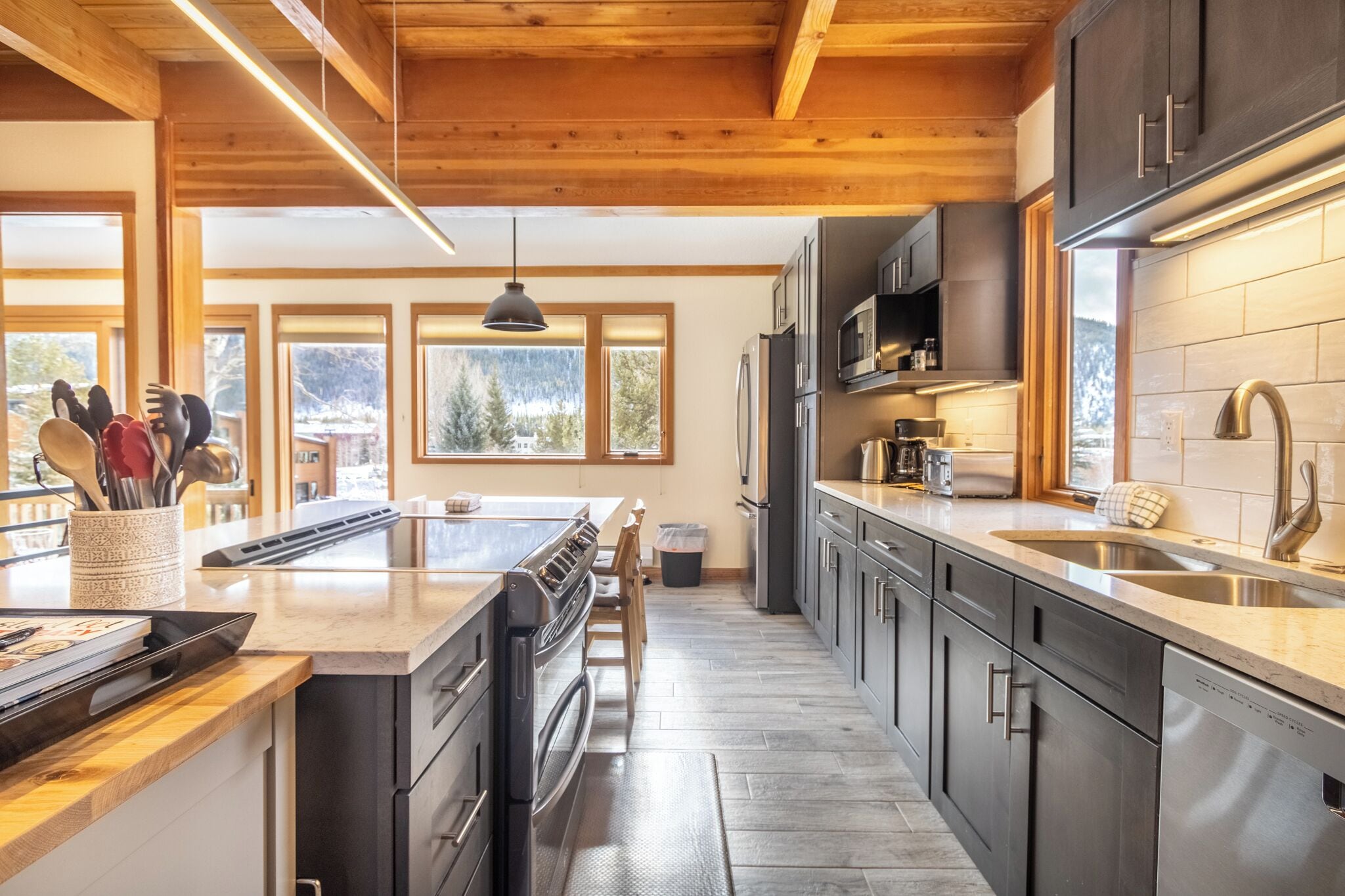 A modern kitchen with wooden beams, stainless steel appliances, and large windows offering a view of the outdoors.