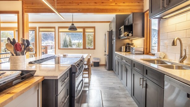 A modern kitchen with wooden beams, stainless steel appliances, and large windows offering a view of the outdoors. - Tennis Townhome #1337 by Summit County Mountain Retreats (Keystone)